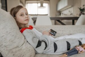A young girl with an insulin pump resting on a couch indoors in casual attire.