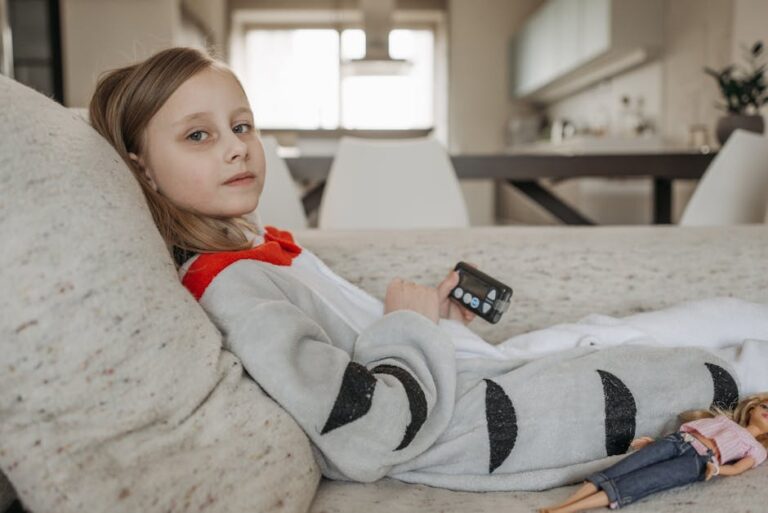 A young girl with an insulin pump resting on a couch indoors in casual attire.