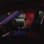 Bearded man in car at night, captured in dramatic lighting.
