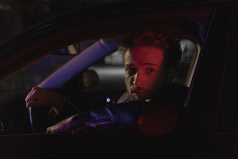 Bearded man in car at night, captured in dramatic lighting.