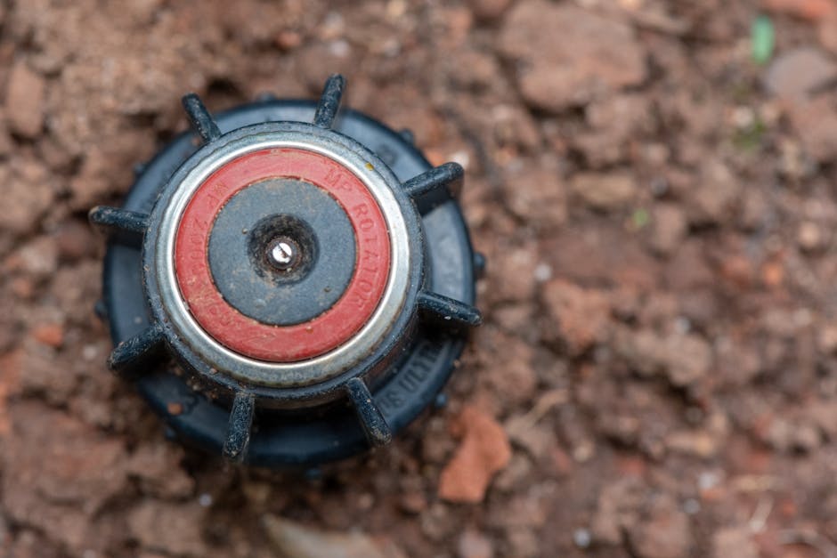 Close-up image of a garden sprinkler head embedded in soil, ideal for landscaping themes.