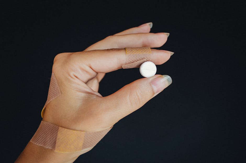 A hand wrapped in bandages holding a white pill against a dark background.