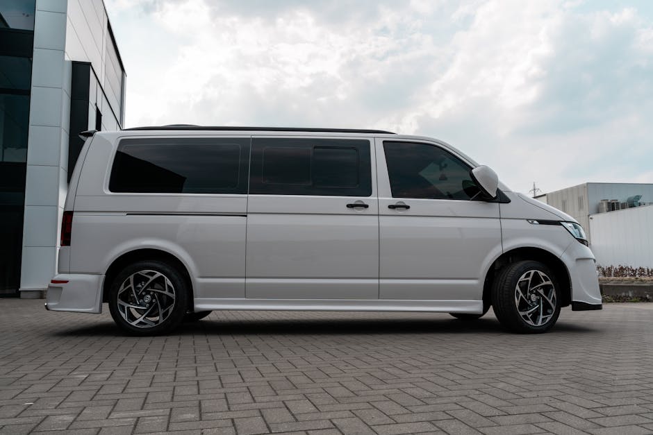 A modern white van parked outdoors on stone pavement with visible rims and side mirror.