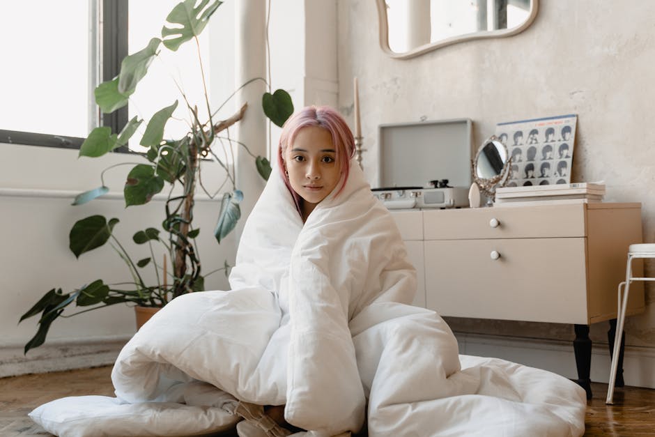 Young woman with pink hair wrapped in a blanket, enjoying a calm moment indoors.