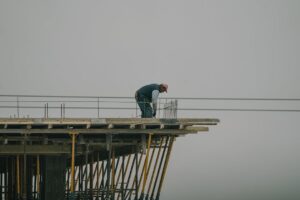 A construction worker bends over rebar on a high framework under a foggy sky in Denizli, Türkiye.