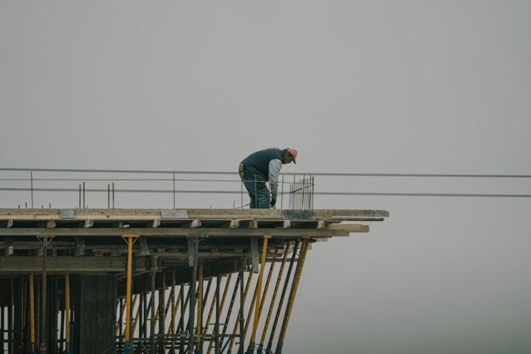 A construction worker bends over rebar on a high framework under a foggy sky in Denizli, Türkiye.
