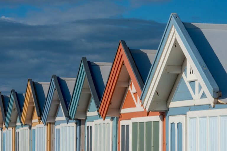 Vibrant row of beach huts with blue sky and clouds creates a picturesque coastal scene.