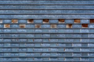 Close-up of a textured metal garage door with a unique brick-like pattern and weathered surface.