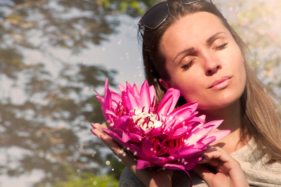 A beautiful woman with closed eyes holding pink lotus flowers in sunlight.