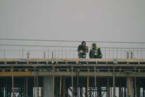 Two construction workers on a building site in Denizli, Türkiye, working under overcast skies.