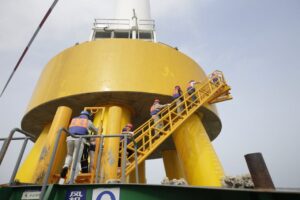 Workers in safety gear ascending a yellow industrial structure via a ladder.