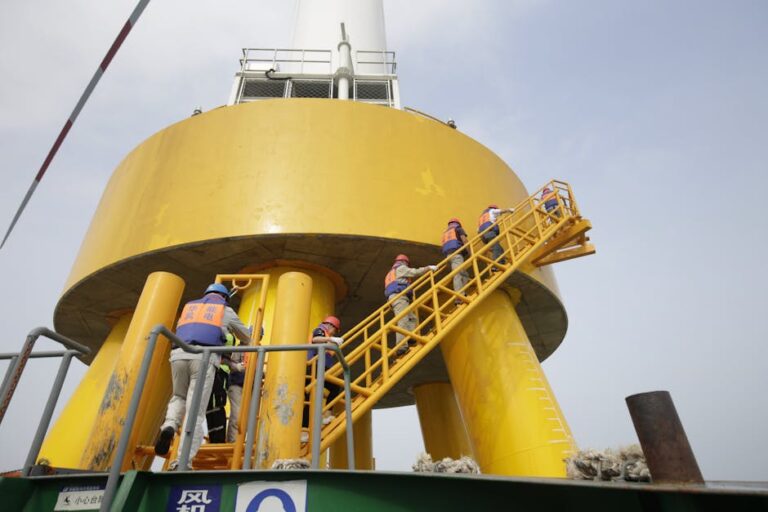 Workers in safety gear ascending a yellow industrial structure via a ladder.