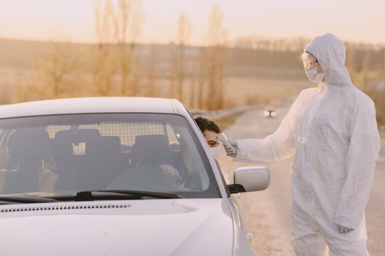 Healthcare worker in protective suit conducting drive-through COVID-19 test outdoors.