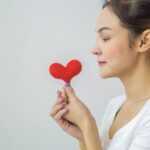 Side view of a young woman holding a red heart symbol, promoting love and wellness.