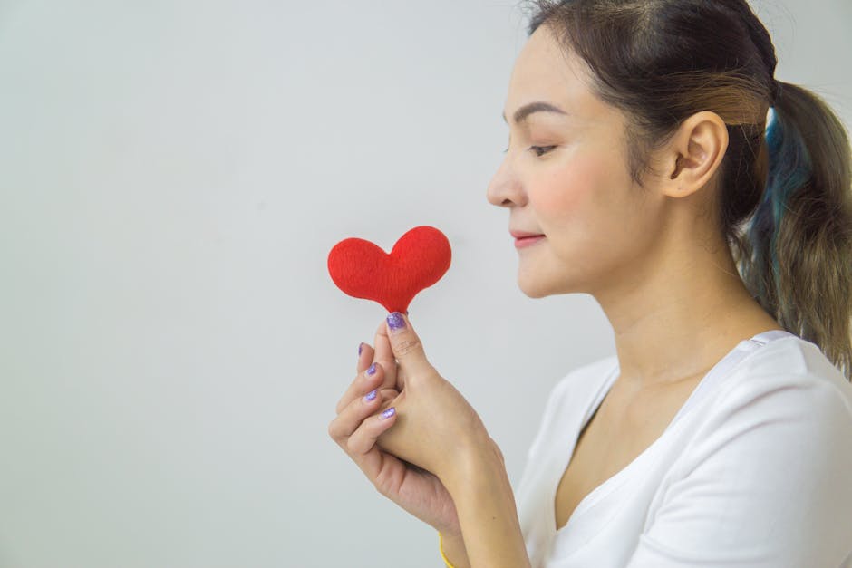 Side view of a young woman holding a red heart symbol, promoting love and wellness.