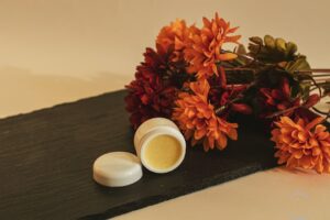 Close-up of orange flowers and cosmetic cream on slate, evoking fall aesthetics.
