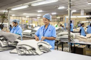 Smiling workers in a textile factory folding garments, showcasing teamwork and industrial efficiency.