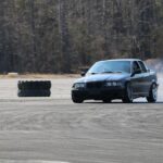 Dynamic shot of a car performing a high-speed drift on an outdoor track, leaving a trail of smoke.