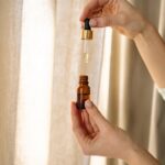 Close-up of hands holding a dropper and amber bottle for skincare product.