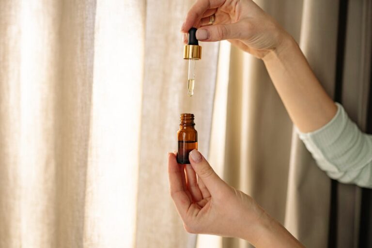 Close-up of hands holding a dropper and amber bottle for skincare product.