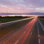 Long exposure highway shot showcasing vibrant car light trails against a sunset sky.