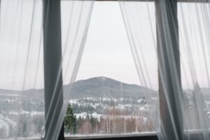 A serene winter landscape framed by sheer curtains, showcasing snow-covered mountains and forests.