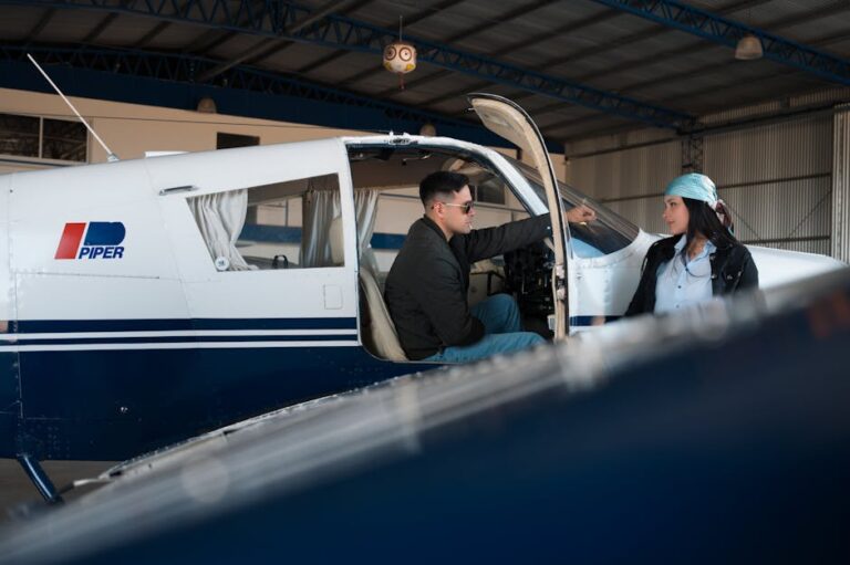 Two individuals conversing by a small aircraft in a hangar, suggesting aviation and teamwork.