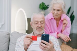 Elderly couple using smartphone and credit card for online shopping at home.