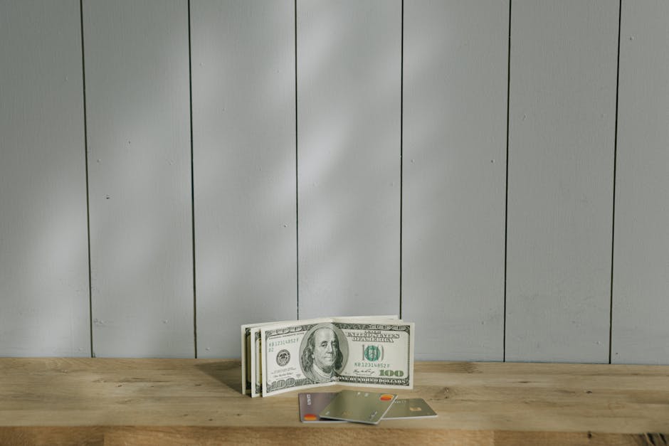 A stack of hundred-dollar bills and credit cards on a wooden surface with a neutral background.