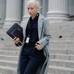 Professional woman in formal attire walking down courthouse steps holding folders outdoors.