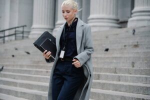 Professional woman in formal attire walking down courthouse steps holding folders outdoors.
