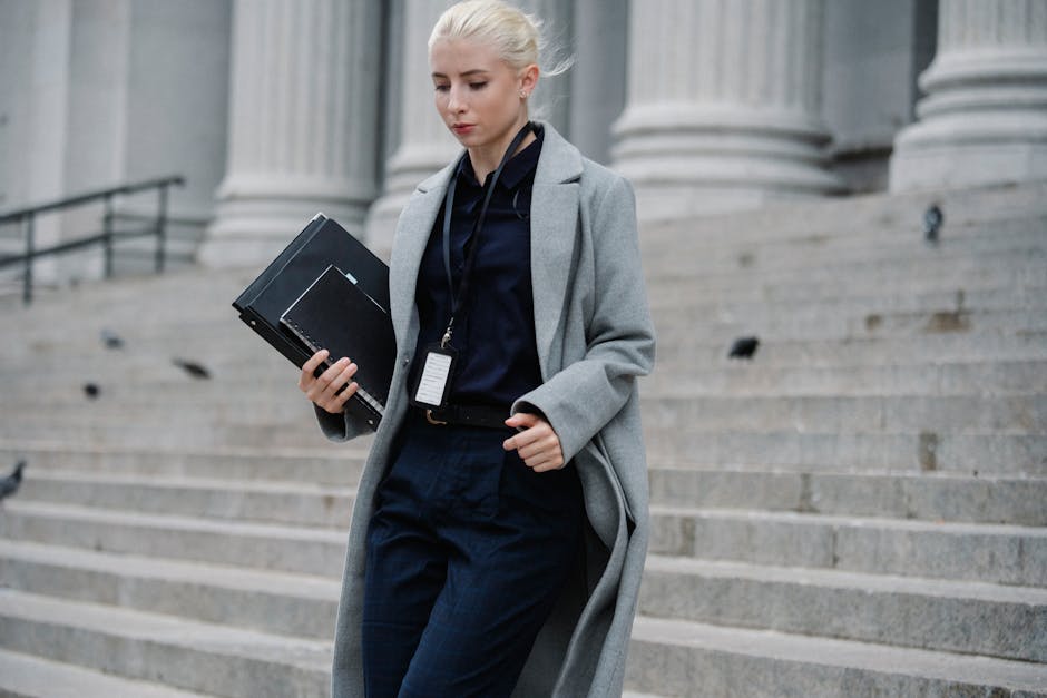 Professional woman in formal attire walking down courthouse steps holding folders outdoors.